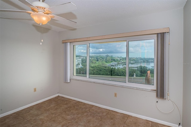 spare room with ceiling fan, a water view, a healthy amount of sunlight, and a textured ceiling