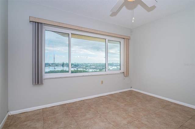 empty room featuring light tile patterned floors, a water view, plenty of natural light, and ceiling fan