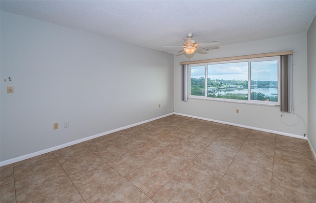 spare room featuring ceiling fan, light tile patterned floors, a water view, and a textured ceiling