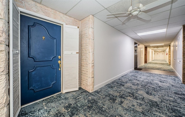 entryway featuring ceiling fan, a drop ceiling, carpet, and brick wall