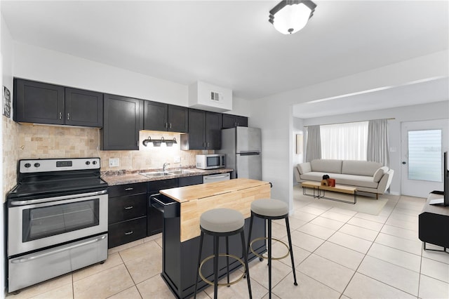 kitchen with appliances with stainless steel finishes, decorative backsplash, light stone countertops, a breakfast bar area, and sink