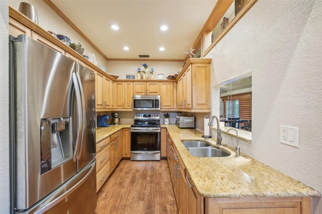 kitchen with stainless steel appliances, a sink, light stone countertops, light wood finished floors, and crown molding