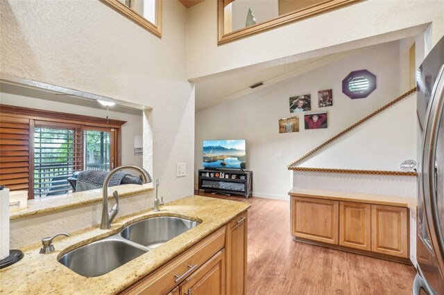 kitchen with lofted ceiling, freestanding refrigerator, light stone countertops, light wood-type flooring, and a sink