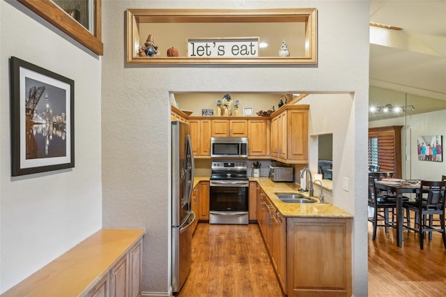 kitchen with light stone counters, wood finished floors, a sink, appliances with stainless steel finishes, and brown cabinetry