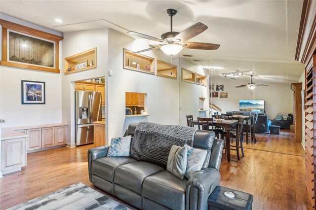 living area with attic access, vaulted ceiling, light wood finished floors, and ceiling fan