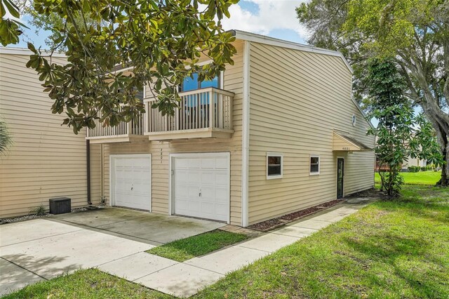 view of side of home with a garage, driveway, a lawn, and a balcony