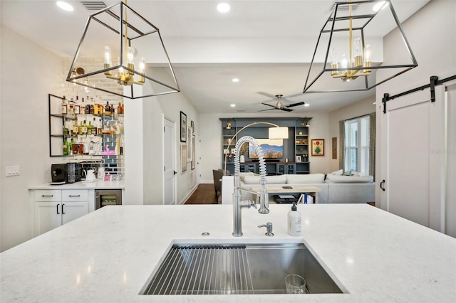 kitchen featuring ceiling fan, sink, wood-type flooring, a barn door, and decorative light fixtures