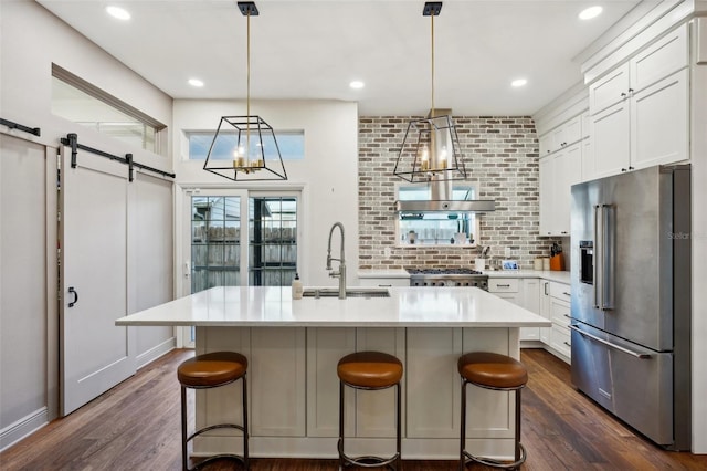 kitchen featuring sink, stainless steel appliances, dark wood-type flooring, a barn door, and an island with sink