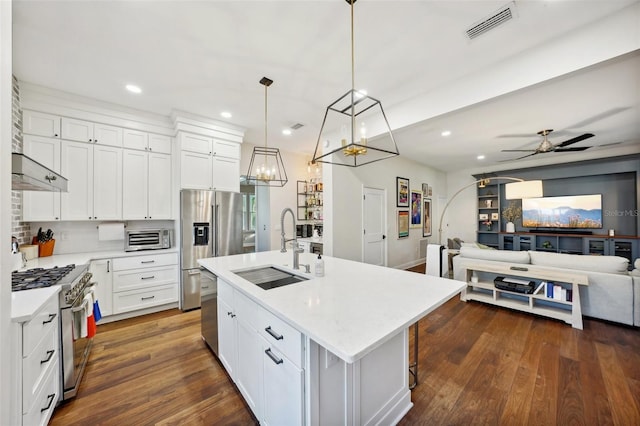 kitchen with dark hardwood / wood-style flooring, stainless steel appliances, hanging light fixtures, and an island with sink