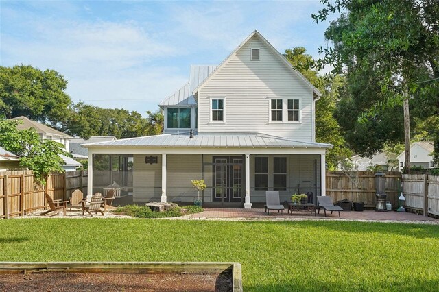 rear view of property featuring a yard, an outdoor fire pit, a patio area, and a sunroom