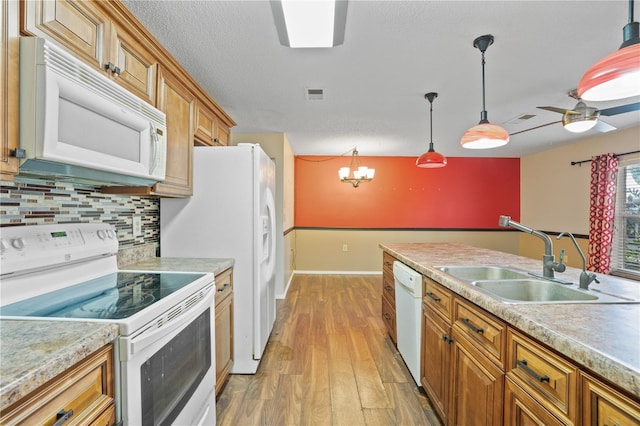 kitchen with white appliances, sink, pendant lighting, light wood-type flooring, and ceiling fan with notable chandelier