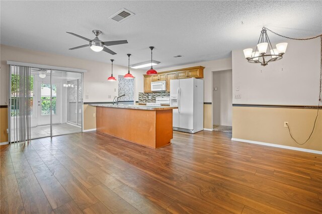 kitchen featuring dark wood-type flooring, light stone countertops, pendant lighting, a textured ceiling, and white appliances