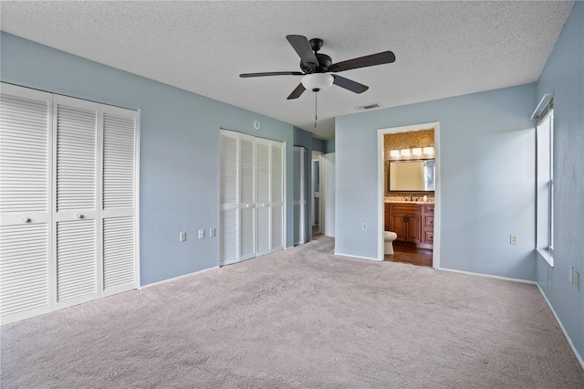 unfurnished bedroom with multiple closets, carpet, ensuite bathroom, a textured ceiling, and ceiling fan