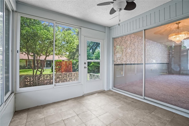 unfurnished sunroom featuring ceiling fan with notable chandelier and plenty of natural light