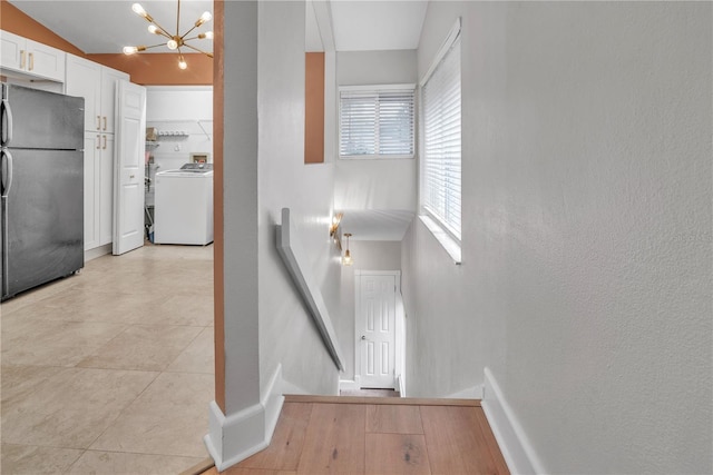 interior space with a chandelier, decorative light fixtures, black refrigerator, washer / dryer, and white cabinets