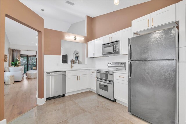 kitchen with vaulted ceiling, appliances with stainless steel finishes, decorative backsplash, white cabinets, and sink