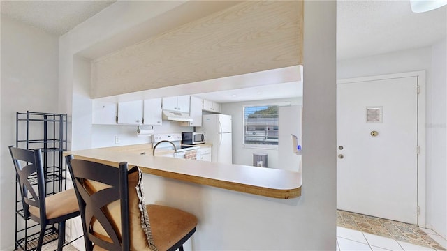 kitchen featuring kitchen peninsula, appliances with stainless steel finishes, white cabinetry, a kitchen bar, and light tile patterned flooring