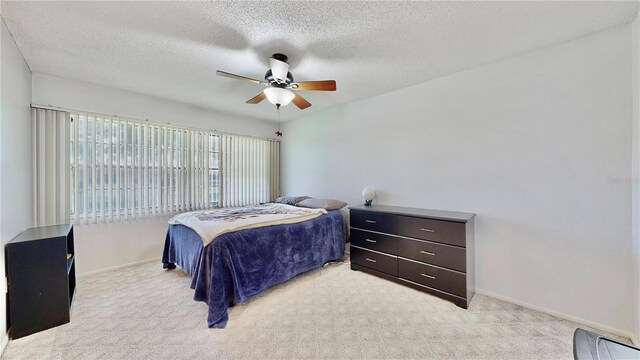 bedroom with a ceiling fan, light colored carpet, baseboards, and a textured ceiling