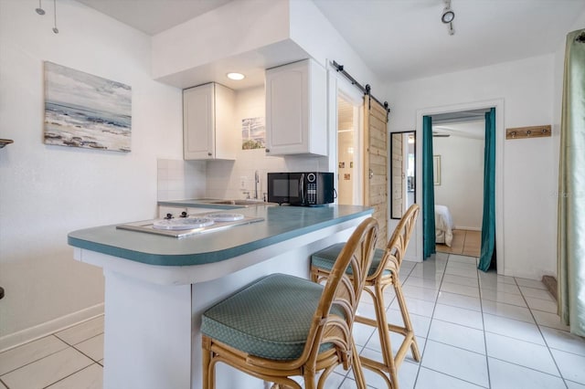 kitchen featuring tasteful backsplash, sink, white cabinetry, a barn door, and light tile patterned flooring