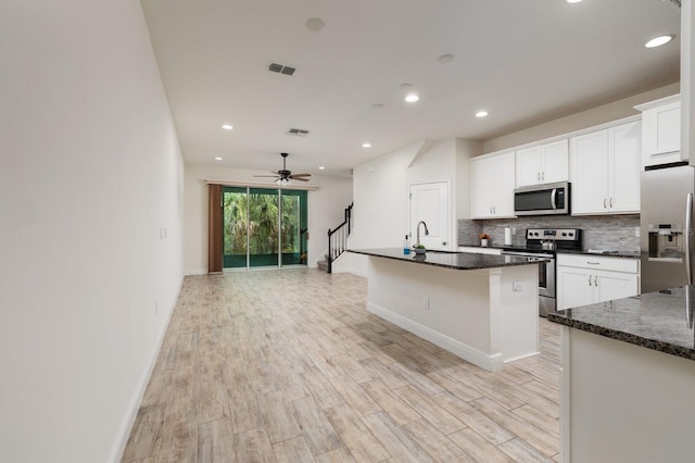 kitchen featuring appliances with stainless steel finishes, light hardwood / wood-style floors, white cabinetry, ceiling fan, and a center island with sink