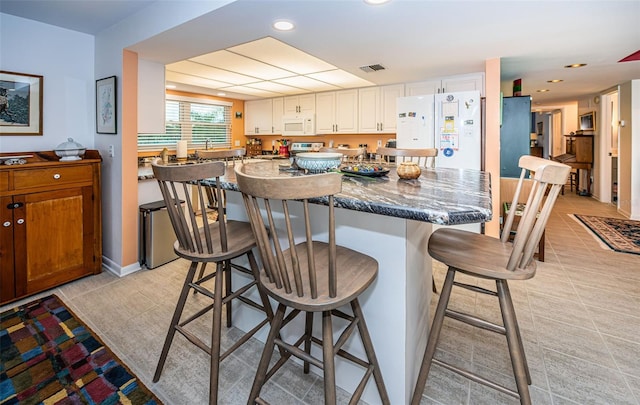 kitchen featuring a kitchen bar, white appliances, white cabinetry, and dark stone countertops