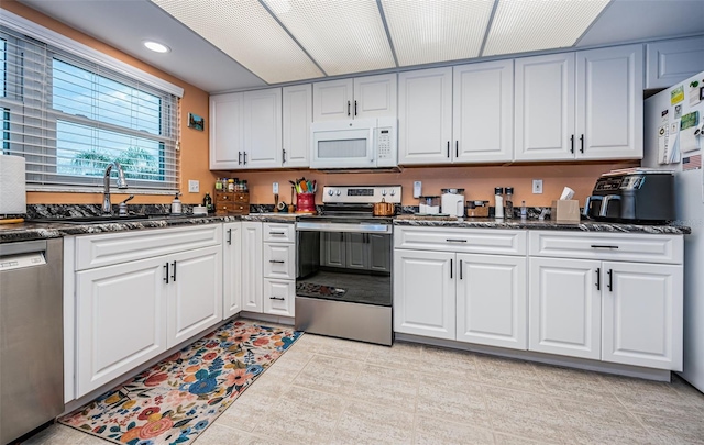 kitchen featuring white cabinetry, stainless steel appliances, dark stone counters, sink, and light tile patterned floors