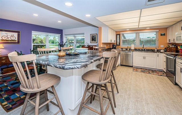 kitchen with stainless steel appliances, a kitchen breakfast bar, dark stone counters, white cabinets, and sink