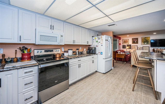 kitchen featuring white cabinets, dark stone counters, and white appliances