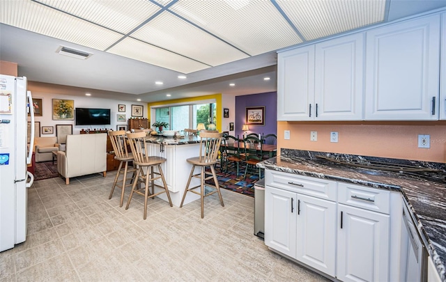 kitchen featuring a breakfast bar, dark stone counters, white refrigerator, and white cabinetry