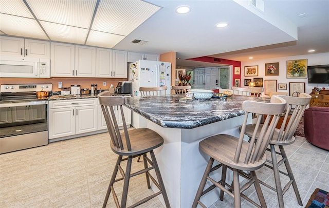 kitchen featuring dark stone countertops, a kitchen island, white appliances, white cabinetry, and a breakfast bar area