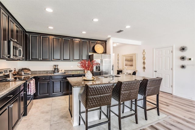 kitchen featuring a kitchen island with sink, light hardwood / wood-style flooring, stainless steel appliances, sink, and stone countertops