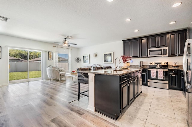 kitchen featuring light stone counters, stainless steel appliances, sink, a kitchen island with sink, and a textured ceiling