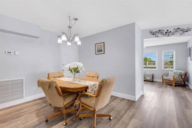 dining space featuring a textured ceiling, an inviting chandelier, and light hardwood / wood-style floors