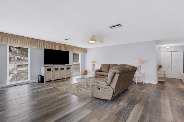 living room featuring dark wood-type flooring, ceiling fan, and a textured ceiling