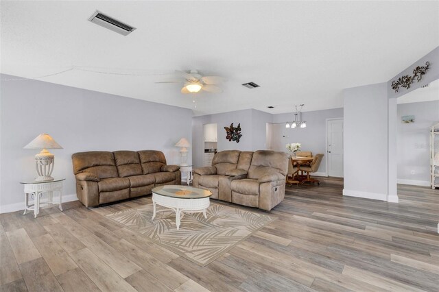 living room with ceiling fan with notable chandelier and light hardwood / wood-style flooring