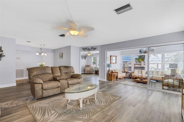 living room with ceiling fan with notable chandelier and hardwood / wood-style floors