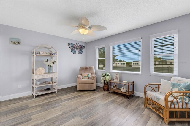 living area featuring ceiling fan, wood-type flooring, and a textured ceiling