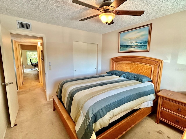 bedroom with a closet, ceiling fan, light colored carpet, and a textured ceiling