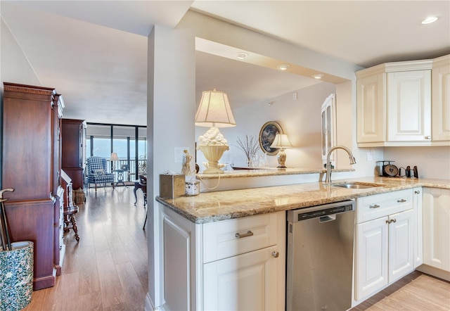 kitchen with light stone countertops, stainless steel dishwasher, sink, light wood-type flooring, and white cabinets