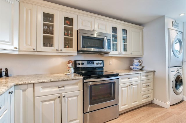 kitchen featuring white cabinetry, light hardwood / wood-style flooring, stainless steel appliances, light stone counters, and stacked washer / drying machine