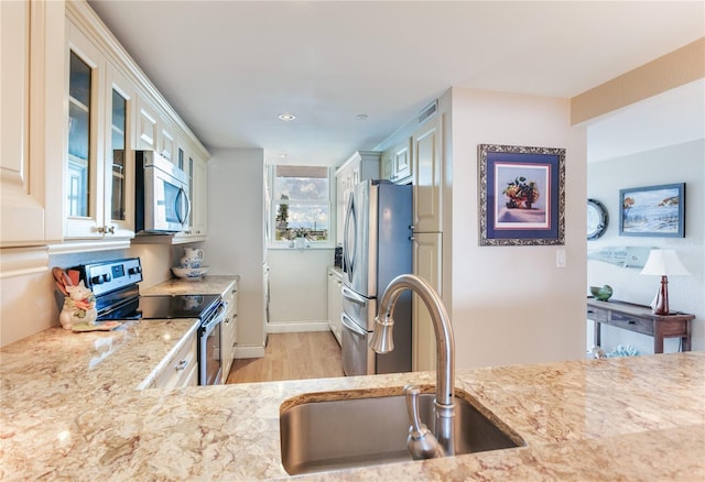 kitchen with light stone counters, stainless steel appliances, light hardwood / wood-style floors, white cabinetry, and sink