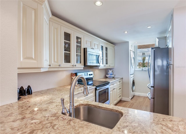 kitchen featuring stacked washer and clothes dryer, light stone countertops, light hardwood / wood-style flooring, appliances with stainless steel finishes, and sink