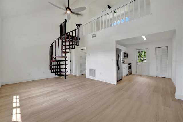 interior space featuring a towering ceiling, light wood-type flooring, and ceiling fan