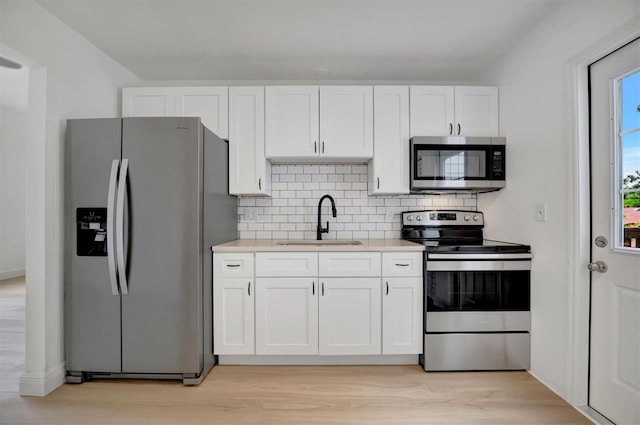 kitchen with appliances with stainless steel finishes, sink, light hardwood / wood-style floors, and white cabinets