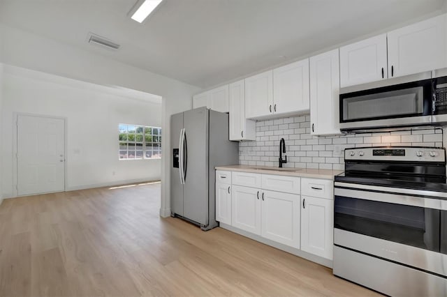 kitchen with stainless steel appliances, tasteful backsplash, white cabinets, sink, and light hardwood / wood-style flooring