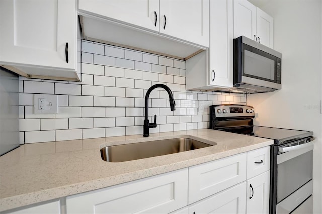 kitchen with sink, light stone countertops, backsplash, white cabinets, and appliances with stainless steel finishes