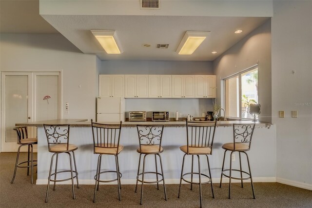 kitchen with white refrigerator, kitchen peninsula, a kitchen breakfast bar, and carpet