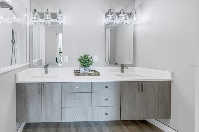 bathroom with double vanity, walk in shower, a sink, and wood finished floors