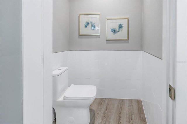 bathroom featuring wood finished floors, toilet, and tile walls