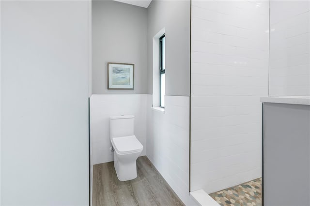 bathroom with toilet, a wainscoted wall, wood finished floors, walk in shower, and tile walls